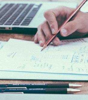 main qui écrit avec un crayon de papier sur une feuille